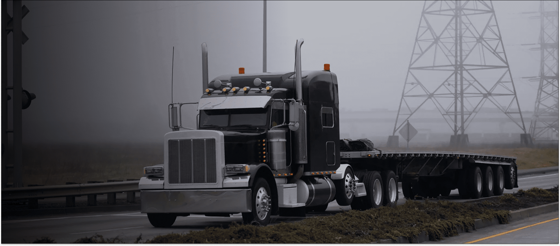 A large black semi-truck parked on a foggy road.